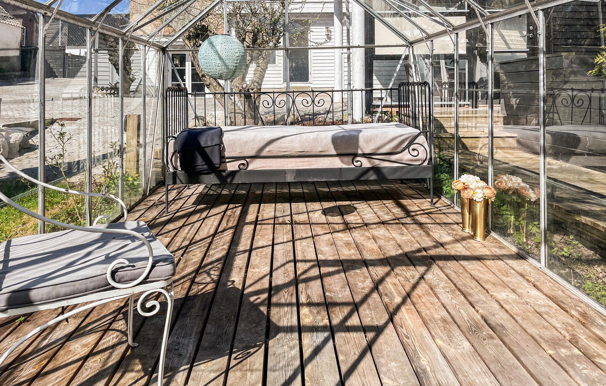 A greenhouse with a wooden deck, a bench, and a table with flowers.