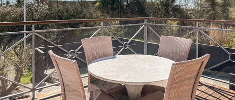 A round table with wicker chairs on a deck with a metal railing.