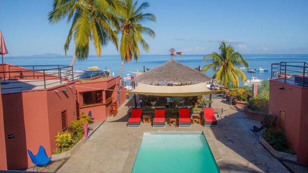 A pool area with lounge chairs, a thatched-roof structure, and palm trees. - Hotel Residence Sarimanok (Nosy Be)