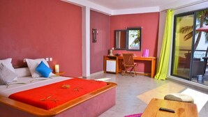 A hotel room with a bed, desk, chair, and a view of the ocean through a large window. - Hotel Residence Sarimanok (Nosy Be)
