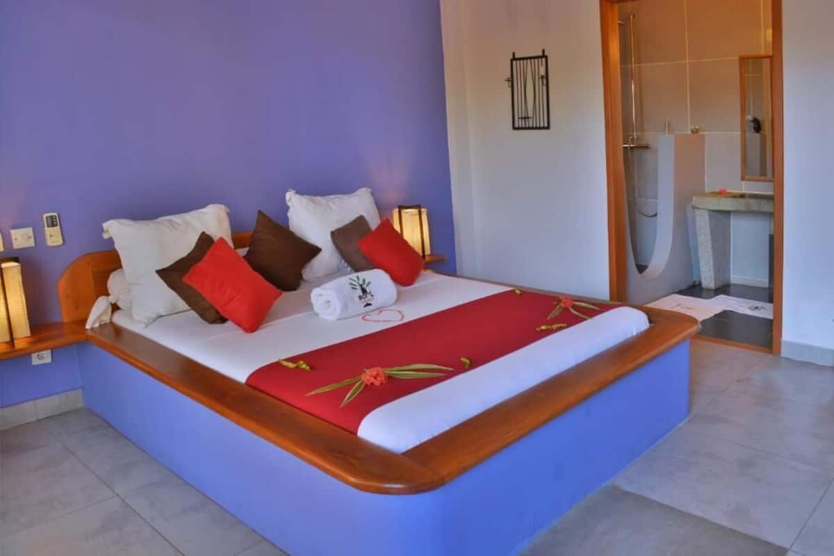 A bedroom with a bed, pillows, a bedside table, a nightstand, a bathroom with a shower, and a sink.