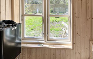 Habitación con ventana que da a un jardín, una barbacoa Harvia y un banco de madera.