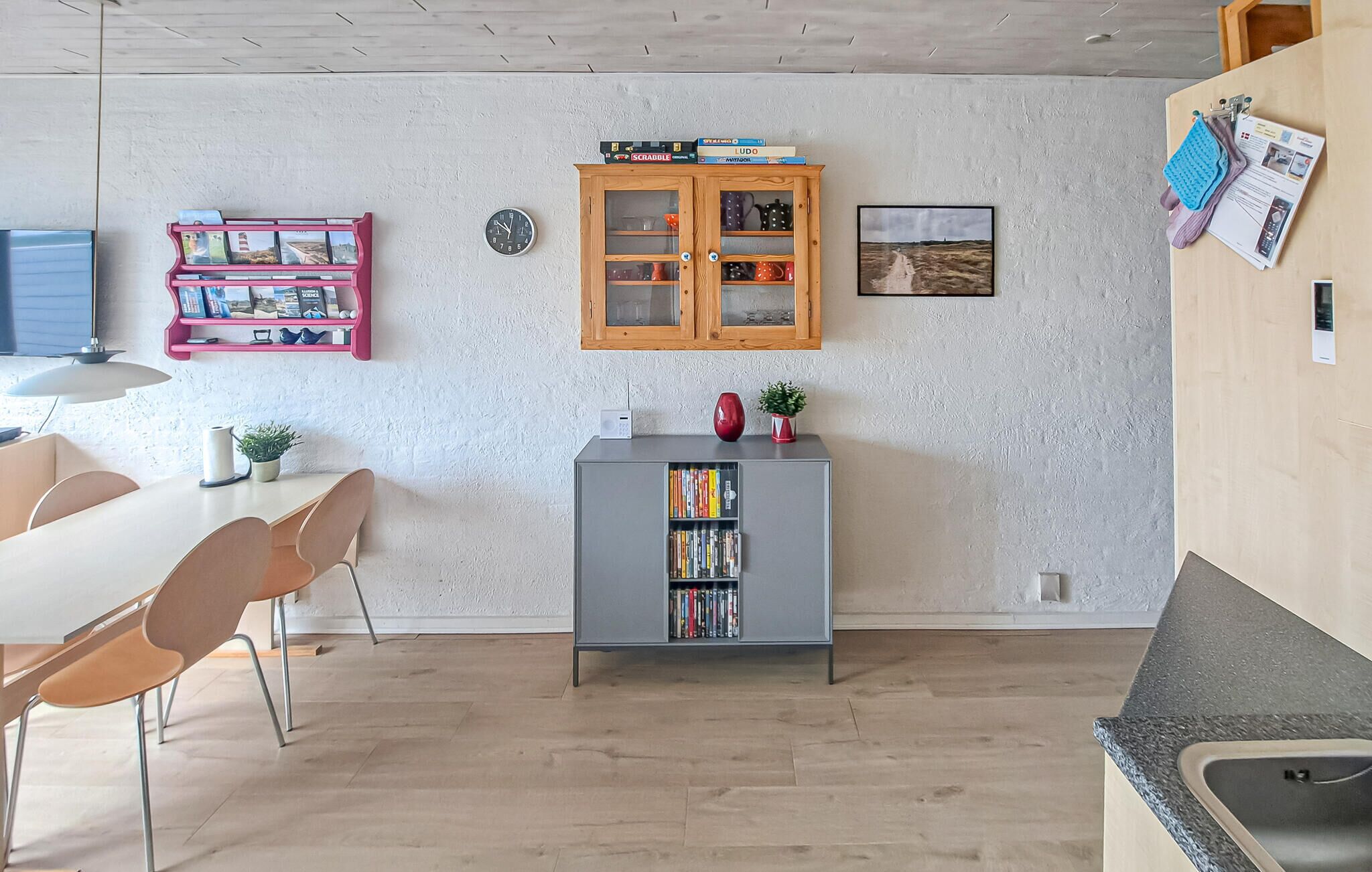 A modern kitchen with a grey cabinet, wooden cabinets above, and a dining area with chairs and a table.