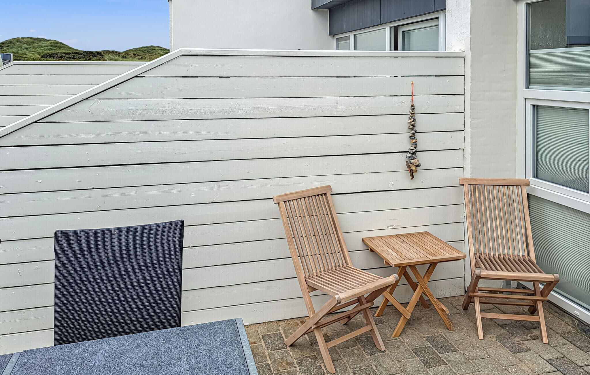 Una terraza en la azotea con dos sillas de madera y una mesa pequeña, un tapete tejido y un adorno en la pared.