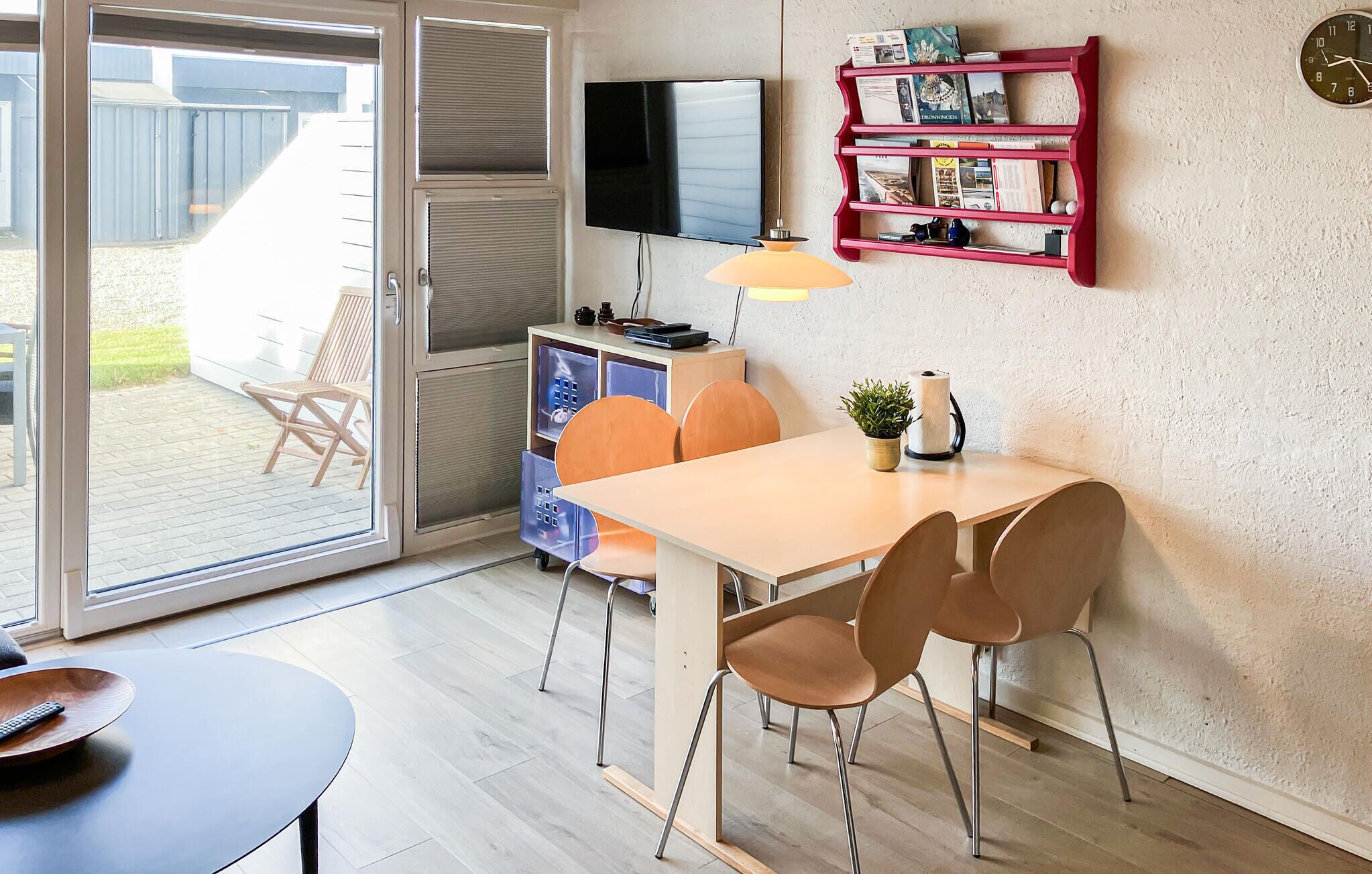 Une cuisine moderne équipée d’un téléviseur, d’une étagère rouge contenant des livres, d’une horloge et d’une porte coulissante donnant sur un patio.