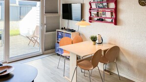 A modern kitchen with a TV, a red shelf with books, a clock, and a sliding door to a patio. - Amazing home in Vestervig with sauna (Vestervig)