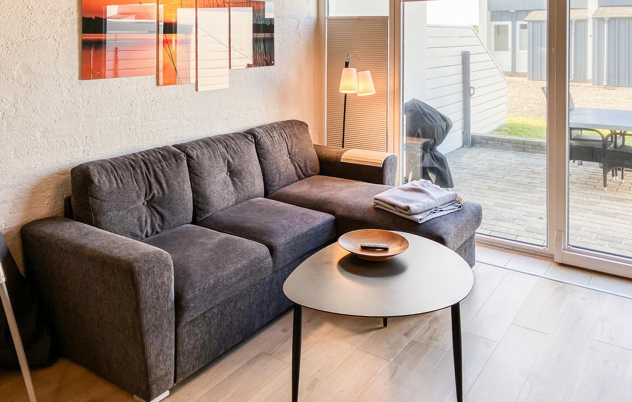 A modern living room with a grey sofa, a round coffee table, and a large window offering a view of the outdoors.