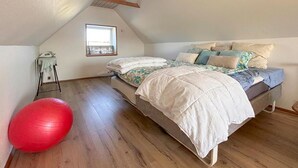 Une chambre avec un plafond en pente, un lit avec de nombreux oreillers, un lampadaire et un ballon rouge pour faire de l’exercice.