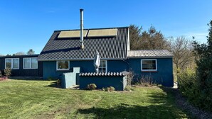 Une maison de plain-pied avec un toit en pente, une cheminée et une petite dépendance attenante recouverte de tuiles.