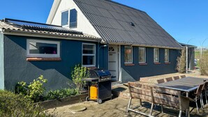 Une maison avec un toit en pente, une porte d’entrée et un patio comprenant une table et des chaises.