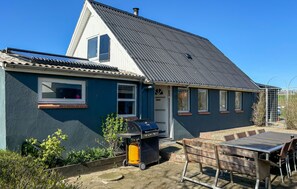 A house with a sloped roof, a front door, and a patio area with a table and chairs.