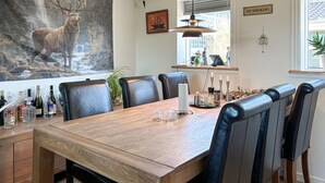 Un coin repas avec une table en bois, des chaises en cuir noir, une suspension et un tableau représentant un cerf accroché au mur.
