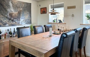 A dining area with a wooden table, black leather chairs, a hanging pendant light, and a painting of a deer on the wall.