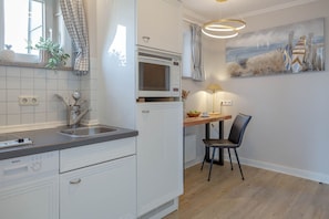 A kitchen with white cabinets, a Bosch dishwasher, a microwave, and a wooden dining table with a chair. - Beach Suite - Holiday apartment "Beach Suite" in Westerland (Sylt)