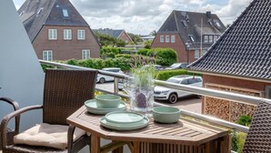 Ein Balkon mit Korbmöbeln, einem Tisch gedeckt mit Tellern und Gläsern, und im Hintergrund eine Aussicht auf Häuser und Autos.