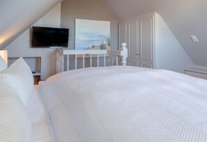 A bedroom with a large bed, a television mounted on the wall, and a painting above the bed. - Heefwai 2-W6 - Heefwai 6 - for two people (Sylt-Ost)