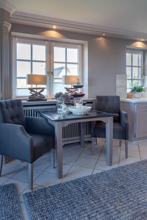 A dining area with a table set for two, a chair, a lamp, and a window with a view. - Heefwai 2-W6 - Heefwai 6 - for two people (Sylt-Ost)