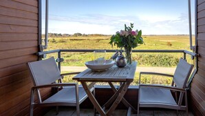 Ein Balkon mit zwei Stühlen, einem Tisch, einer Blumenvase und Blick auf ein grünes Feld.
