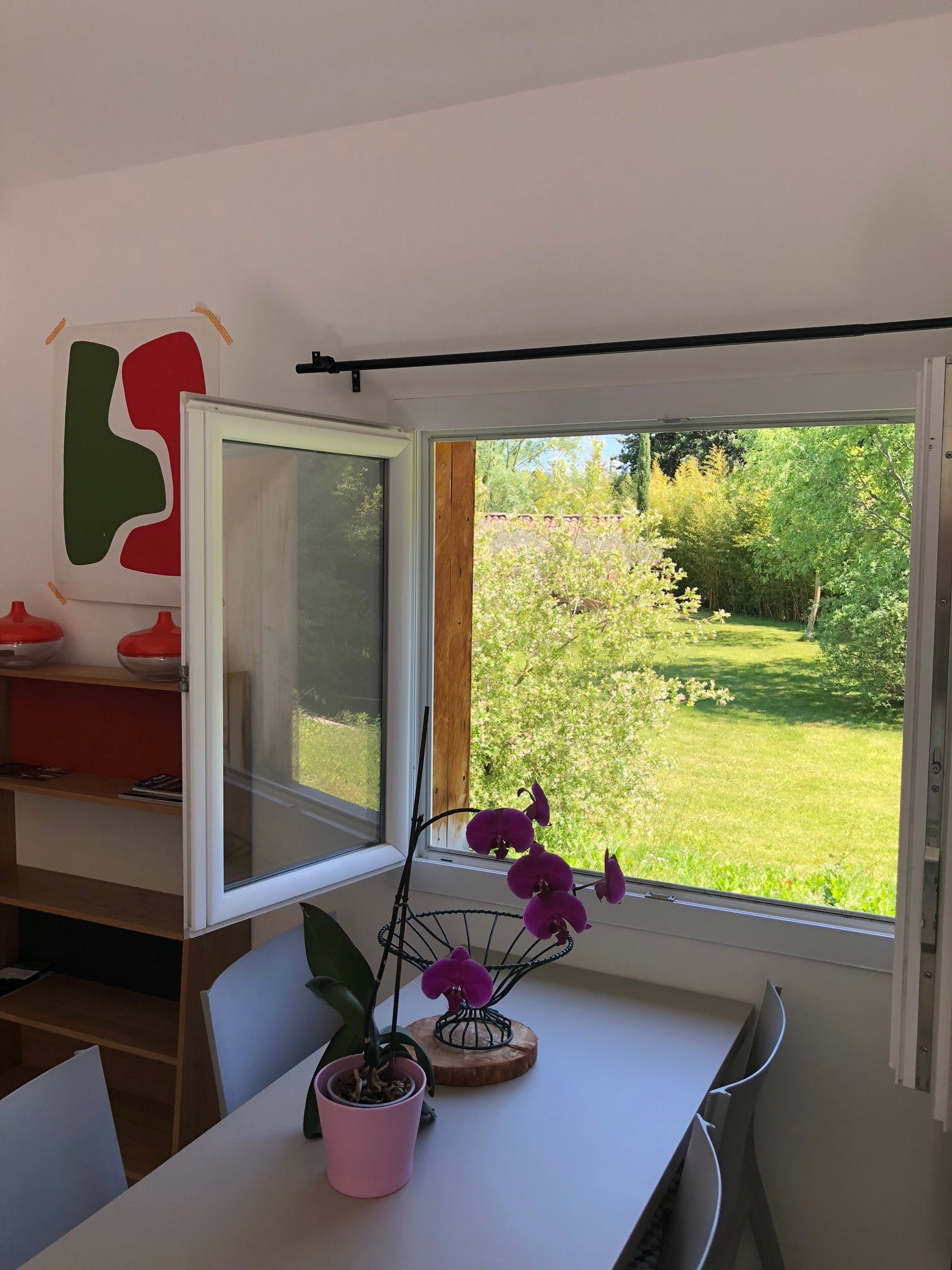 Et værelse med et bord, stole, et vindue med udsigt til en have og en potteplante.