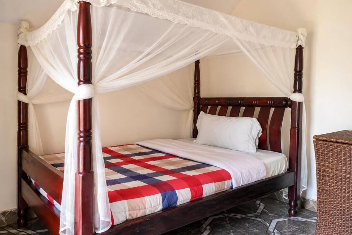 A four-poster bed with a white canopy, a checkered bedspread, and a wicker side table.