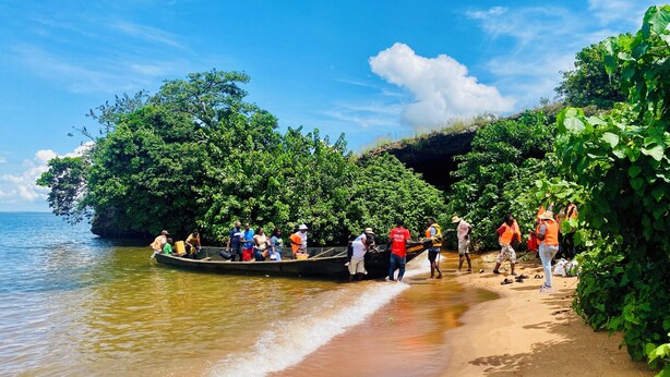 Una playa con un bote lleno de gente, rodeada de exuberante vegetación.
