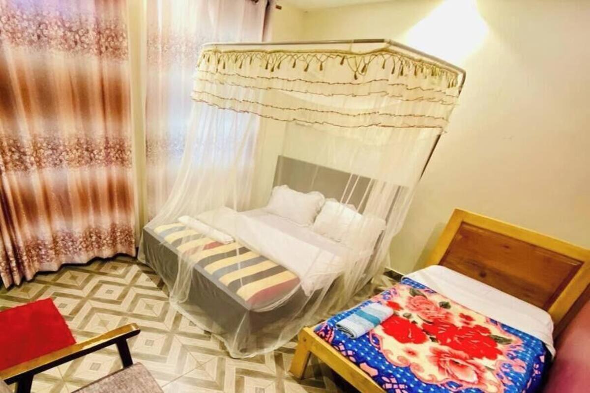 A room with a bed under a canopy, another bed with a floral bedspread, a chair, and a small table.