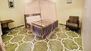 Una habitación con una cama bajo un dosel, una silla, una mesita y suelo con estampado.