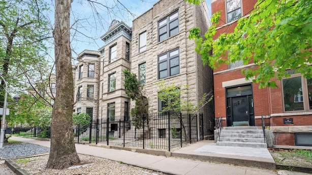 Une rangée de maisons de ville aux façades en pierre et en brique, une clôture en métal noir et un arbre au premier plan.