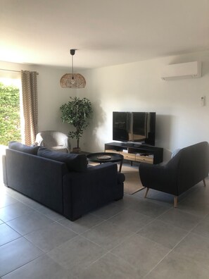 A modern living room with a sofa, armchair, TV, and a potted plant. - House in Le Teich; nature and beaches nearby (Le Teich)