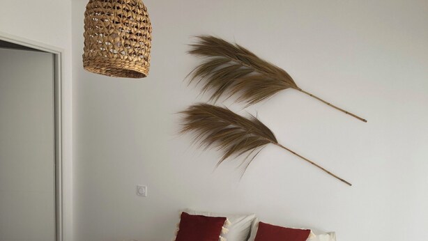 Un dormitorio con cama, lámpara colgante, un taburete de madera y una planta decorativa.