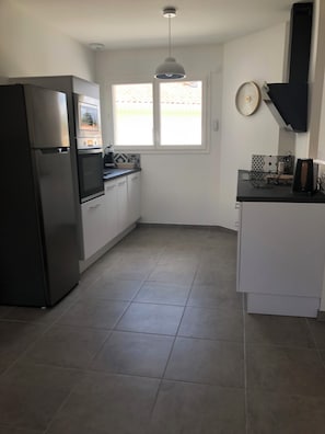 A kitchen with a refrigerator, oven, and a window with a view of a fence. - House in Le Teich; nature and beaches nearby (Le Teich)