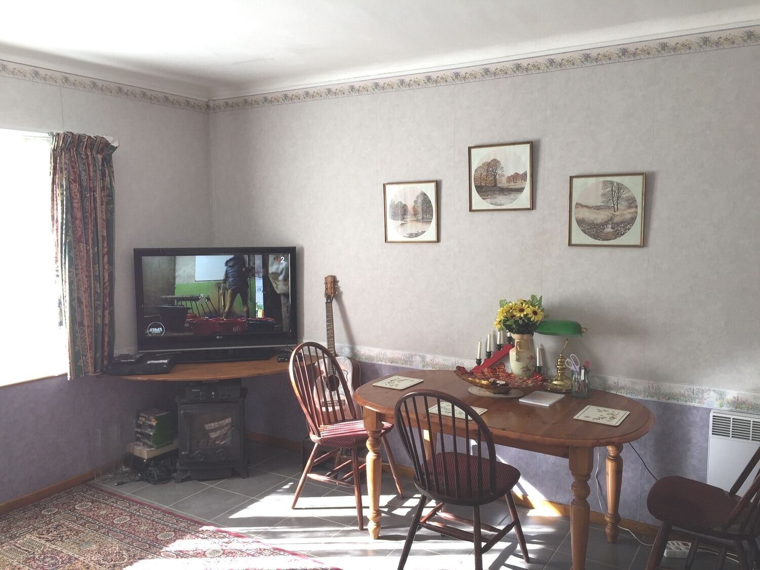 Een eethoek met een televisie, stoelen, een tafel en lijstjes met foto's aan de muur.