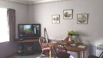 Een eethoek met een televisie, stoelen, een tafel en lijstjes met foto's aan de muur.