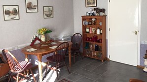 A dining area with a round table, chairs, a wooden cabinet with glassware, framed pictures on the wall, and a white door. - Ground floor cottage Gite with disabled access-Swimming pool-Jacuzzi (Le Poujol-sur-Orb)