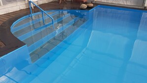 A clear blue swimming pool with a glass bottom, a blue ladder, and two rocks on the edge. - Ground floor cottage Gite with disabled access-Swimming pool-Jacuzzi (Le Poujol-sur-Orb)