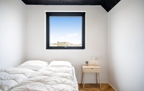 Ein Schlafzimmer mit einem Bett, einem Nachttisch, einer Lampe und einem Fenster mit Blick auf eine Landschaft.