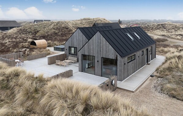 Ein modernes Strandhaus mit geneigtem Dach, großen Fenstern und einer Terrasse mit Gartenmöbeln.