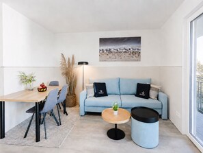 Ein modernes Wohnzimmer mit einer Couch, einem runden Couchtisch, einem Esstisch mit Stühlen und einem großen Fenster.