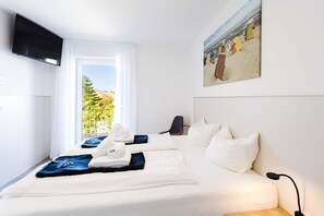 Ein Hotelzimmer mit Bett, Wandfernseher, einem Gemälde und Blick ins Freie.