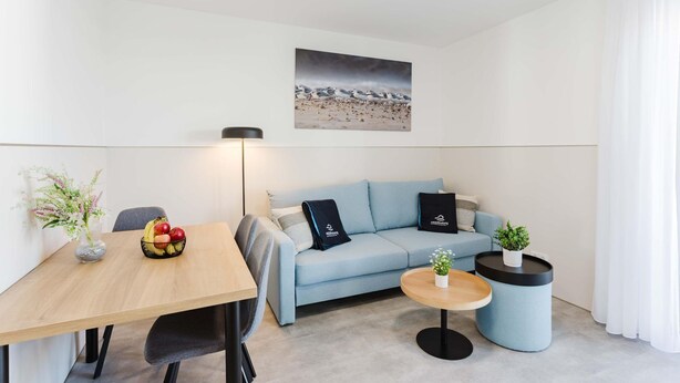 En moderne stue med sofa, spisebord med frugt, lampe og et maleri på væggen.