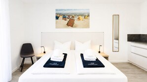 Et hotelværelse med en stor seng, en lænestol, et skrivebord, et spejl og et maleri af en strand.