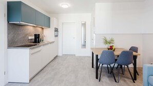 Et moderne køkken med indbygget komfur, kaffemaskine og vask. Der er et spiseområde med et bord og stole, og en lille plante står på bordet.