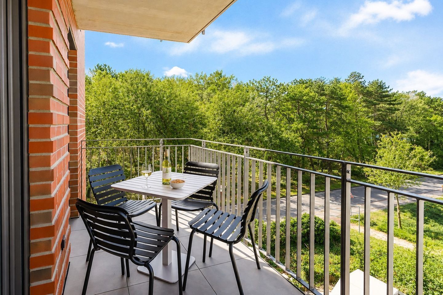 Ein Balkon mit Tisch und Stühlen, einer Weinflasche und einer Schüssel mit Snacks.