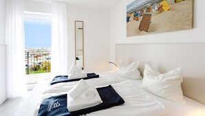 Ett hotellrum med en säng, ett stort fönster, en tavla som föreställer en strandscen och utsikt över staden.