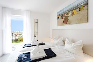 Ein Hotelzimmer mit Bett, großem Fenster, einem Bild mit Strandmotiv und Blick auf die Stadt.