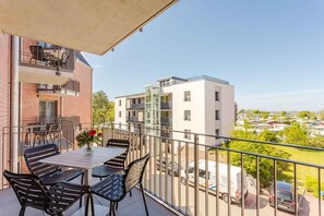 Ein Balkon mit Tisch und Stühlen, einer Blumenvase und Blick auf umliegende Gebäude und geparkte Autos.