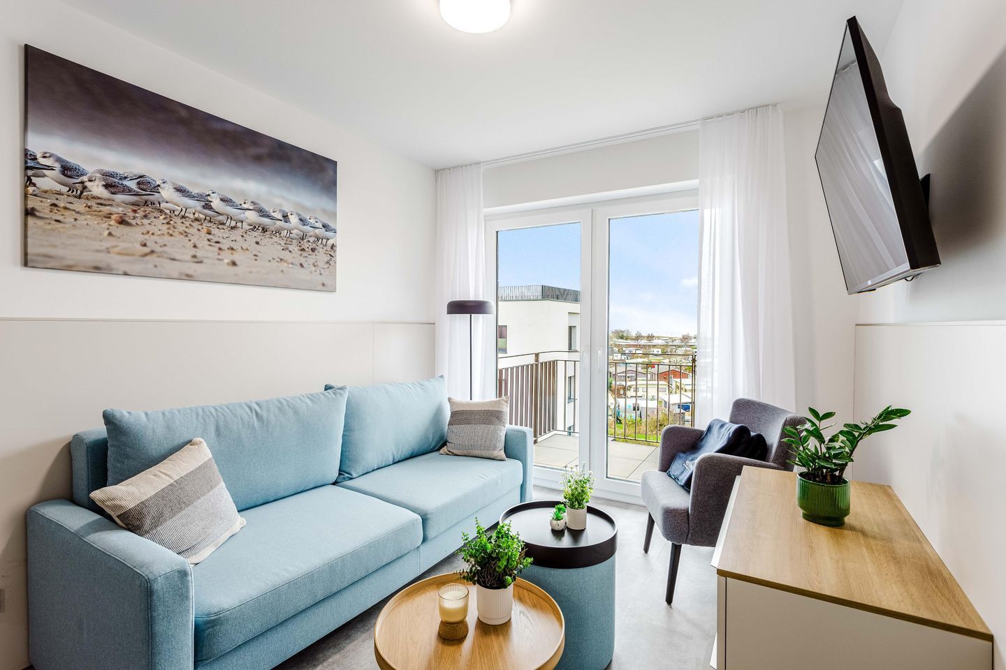 Ein modernes Wohnzimmer mit Sofa, einem Couchtisch mit Pflanzen, einem Fernseher und einem Balkon mit Blick.