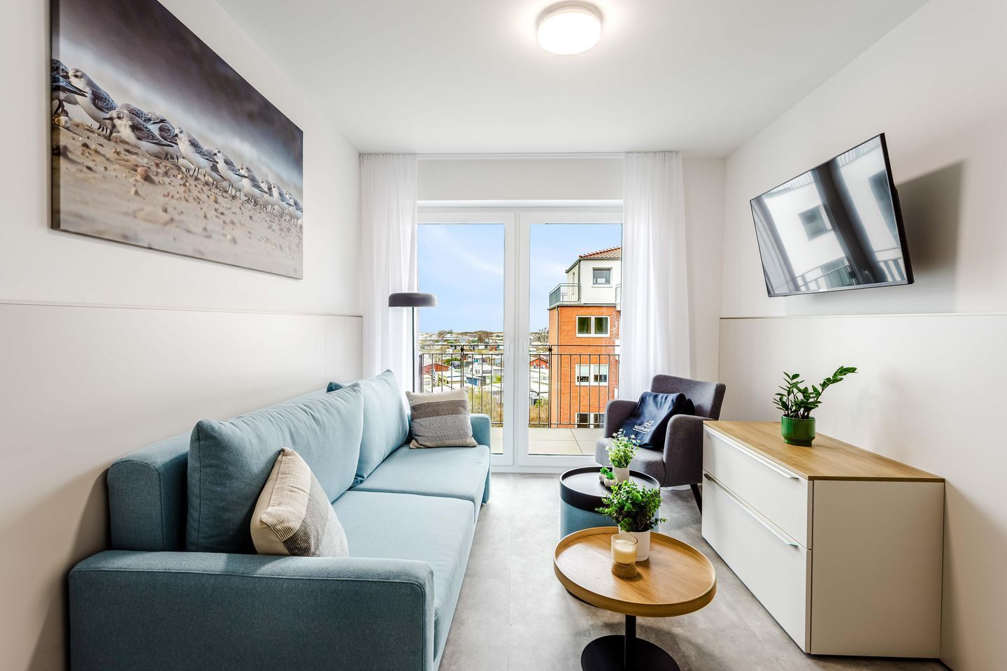 Ein modernes Wohnzimmer mit einer Couch, einem Couchtisch, einem Fernseher und einem Balkon mit Blick auf Gebäude.