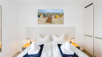 Una habitación de hotel con una cama, dos mesitas de noche, una obra de arte en la pared que representa una playa y un armario.