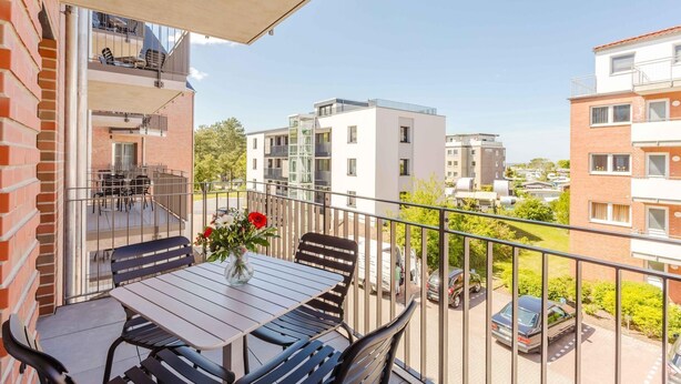 A balcony with a table and chairs, a flower vase, and a view of surrounding buildings. - MEERholung Vacation Rental 2.8 with Balcony, Just 400 m from the Sea - MEERholung House (Cuxhaven)